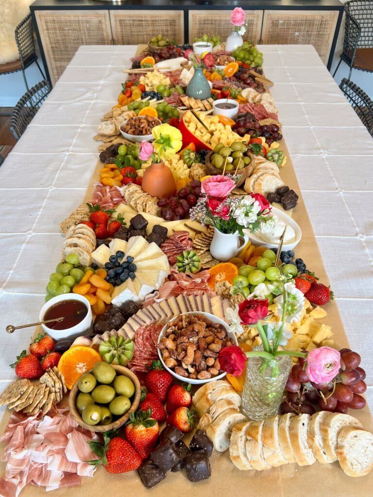 A long grazing table with fruit, cheeses, and flowers