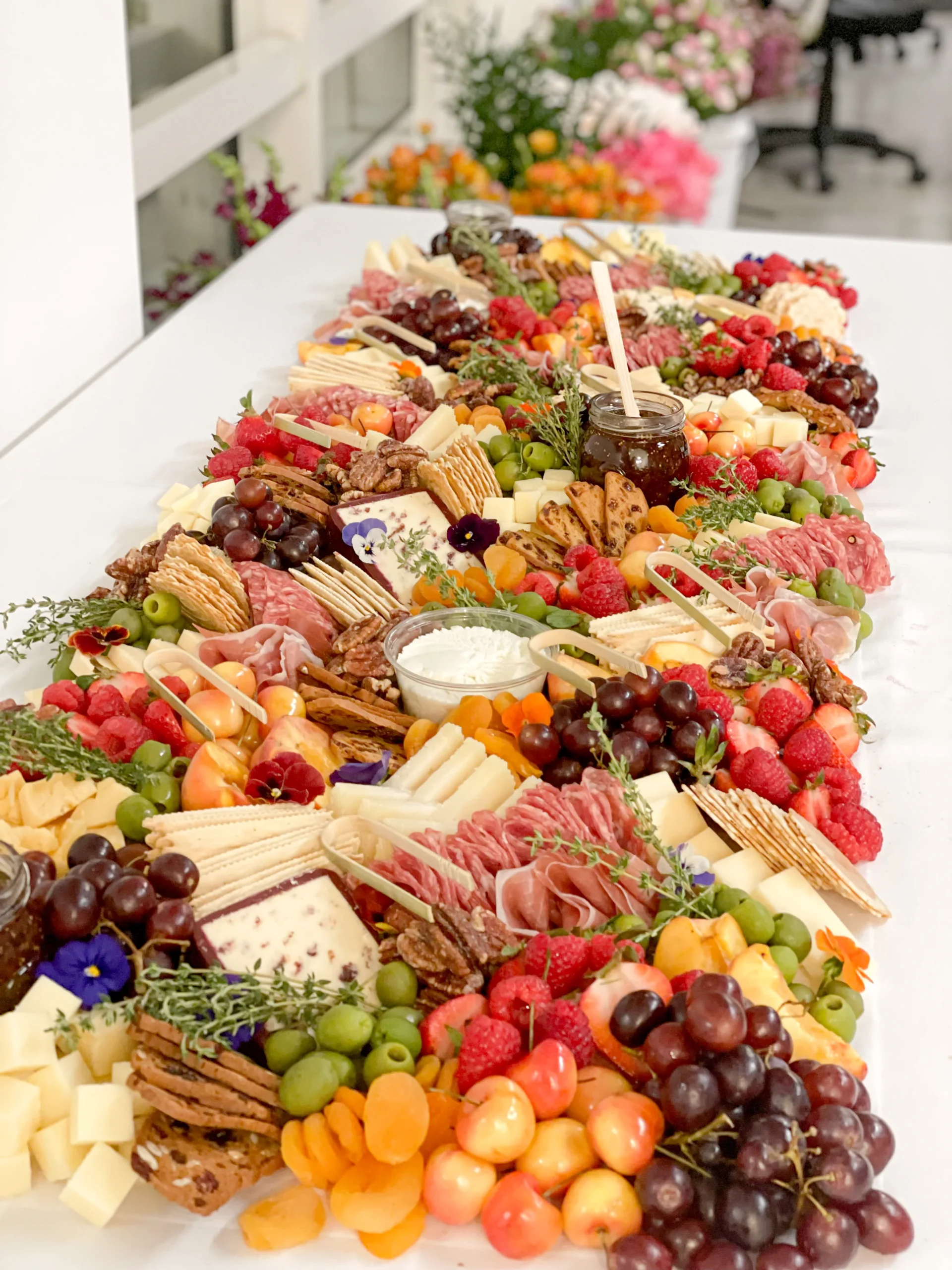 A grazing table with cheeses, fruit, crackers, and flowers